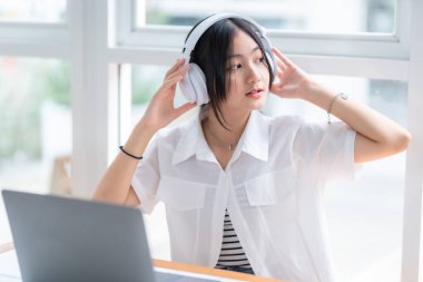 Şirin gülüşler Asyalı, kulaklık takan, müzik dinleyen, kulaklık takan, kafede çalışan bilgisayarlı çekici bir kız. Çevrimiçi eğitim, gelişim konsepti..