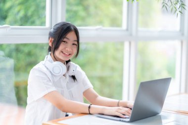 Şirin gülümsemeler Asyalı çekici, küçük sevimli kız kulaklık takan, kafede çalışan dizüstü bilgisayarı kullanan. Çevrimiçi eğitim, gelişim konsepti..