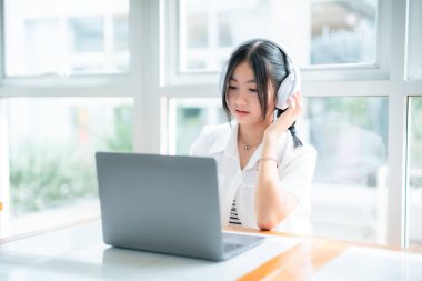 Şirin gülüşler Asyalı, kulaklık takan, müzik dinleyen, kulaklık takan, kafede çalışan bilgisayarlı çekici bir kız. Çevrimiçi eğitim, gelişim konsepti..