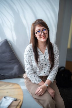 Güzel, mutlu Asyalı bir kadının portresi. Oturma odasındaki rahat koltukta dinleniyor.