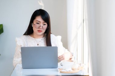 Asyalı serbest çalışanlardan memnun. İş kadını. Kablosuz kulaklık takıyor. Laptop bilgisayarıyla çalışıyor.