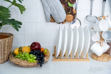 Raflara yerleştirilmiş güzel seramik beyaz kase ve beyaz masadaki mutfakta beyaz cam bardak içme ekipmanı. Düzlük, yemek hazırlama kavramı, arka planda mutfak..