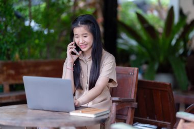 Asyalı genç kız öğrencilerin bilgisayarı kullanarak akıllı telefon kullanarak sohbet etmesinden mutlu. Çevrimiçi eğitim, el kazanma konsepti, serbest çalışan iş kadınları.