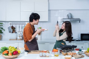 Genç Asyalıyı sevmekten mutluyum. Neşeli bir biftek yemeği hazırlarken akıllı bir telefon al ve bir mutfakta sebzelerle yemek pişirmenin tadını çıkar.