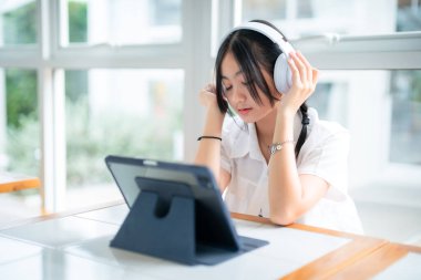 Şirin gülüşler Asyalı, kulaklık takan, müzik dinleyen, kulaklık takan, kafede çalışan bilgisayarlı çekici bir kız. Çevrimiçi eğitim, gelişim konsepti..