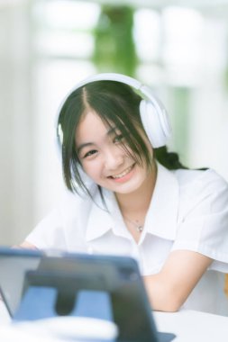 Şirin gülümsemeler Asyalı çekici küçük sevimli kız kulaklık takıyor ve müzik dinliyor kafede çalışan dijital tabletleri kullanıyor. Çevrimiçi eğitim, öğrenim konsepti..