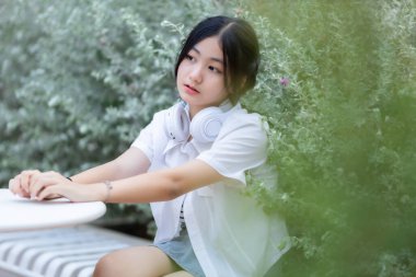 Şirin gülümsemeler Asyalı çekici küçük kız beyaz kablosuz kulaklık takıyor ve müzik dinliyor kafede tatilde en sevdiği sesin tadını çıkarıyor..