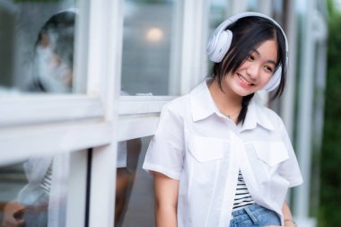 Şirin gülümsemeler Asyalı çekici küçük kız beyaz kablosuz kulaklık takıyor ve müzik dinliyor kafede tatilde en sevdiği sesin tadını çıkarıyor..