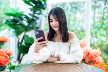 Güzel mutlu Asyalı kadın gezginin modern portresi. Güzel beyaz elbise. Akıllı telefon yaşam tarzını kullanarak mesaj yazmak.