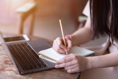 Dizüstü bilgisayarla deftere yazılan notları yakın çekim. Çevrimiçi eğitim, e-öğrenme konsepti, serbest çalışan iş kadınları.