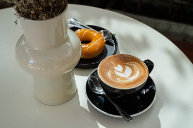 Sütlü sütlü sütlü sütlü sütlü sıcak kahve fincanı ve ahşap masa üzerinde ev yapımı portakallı çörek masası. İş konsepti sırasında bir kafede kahvaltı olarak.