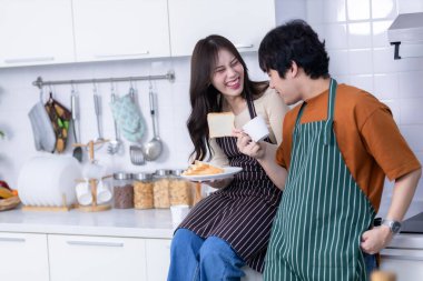 Sevgi dolu genç bir çiftin mutlu portresi. Asyalı neşeli bir bardak ve dilimlenmiş ekmekle ayakta durup yemek pişirmenin ve bir mutfakta ev ya da ev hayatı yaşarken ekmeğin keyfini çıkarmanın mutlu portresi.