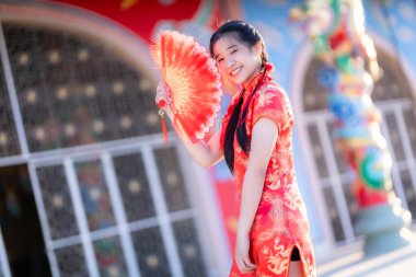 Güzel, şirin bir portre gülümseyen Asyalı genç bir kadın geleneksel Çin cheongsam süslemesi takıyor ve Tayland 'da Çin Yeni Yıl Festivali için Çin Fanning' i düzenliyor.