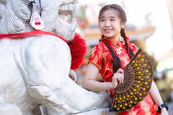 Güzel, şirin bir portre gülümseyen Asyalı genç bir kadın geleneksel Çin cheongsam süslemesi takıyor ve Tayland 'da Çin Yeni Yıl Festivali için Çin Fanning' i düzenliyor.