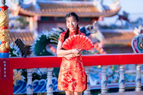 Güzel, şirin bir portre gülümseyen Asyalı genç bir kadın geleneksel Çin cheongsam süslemesi takıyor ve Tayland 'da Çin Yeni Yıl Festivali için Çin Fanning' i düzenliyor.