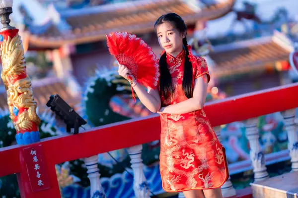Güzel, şirin bir portre gülümseyen Asyalı genç bir kadın geleneksel Çin cheongsam süslemesi takıyor ve Tayland 'da Çin Yeni Yıl Festivali için Çin Fanning' i düzenliyor.
