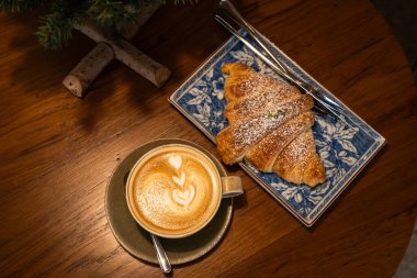 Sütlü sütlü sütlü sütlü sütlü sıcak kahve ve ahşap masa üzerinde kruvasan. Kafedeki bir kafede kahvaltı olarak, iş konsepti sırasında, klasik tarzda.