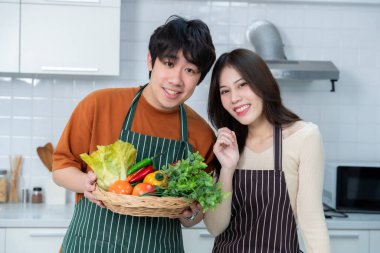 Sevgi dolu genç bir çiftin mutlu portresi. Asyalı neşeli bir şekilde yemek pişirmeyi seviyor. Sebze, et, ekmek pişiriyor.