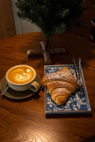 Sütlü sütlü sütlü sütlü sütlü sıcak kahve ve ahşap masa üzerinde kruvasan. Kafedeki bir kafede kahvaltı olarak, iş konsepti sırasında, klasik tarzda.