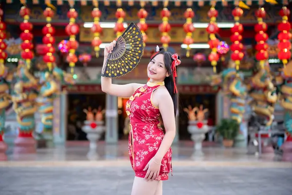 Güzel, şirin bir portre gülümseyen Asyalı genç bir kadın geleneksel Çin cheongsam süslemesi takıyor ve Tayland 'da Çin Yeni Yıl Festivali için Çin Fanning' i düzenliyor.