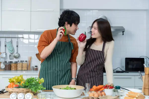 Sevgi dolu genç bir çiftin mutlu portresi. Asyalı neşeli bir şekilde yemek pişirmeyi seviyor. Sebze, et, ekmek pişiriyor.