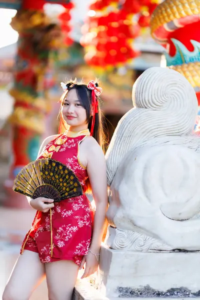 Güzel, şirin bir portre gülümseyen Asyalı genç bir kadın geleneksel Çin cheongsam süslemesi takıyor ve Tayland 'da Çin Yeni Yıl Festivali için Çin Fanning' i düzenliyor.