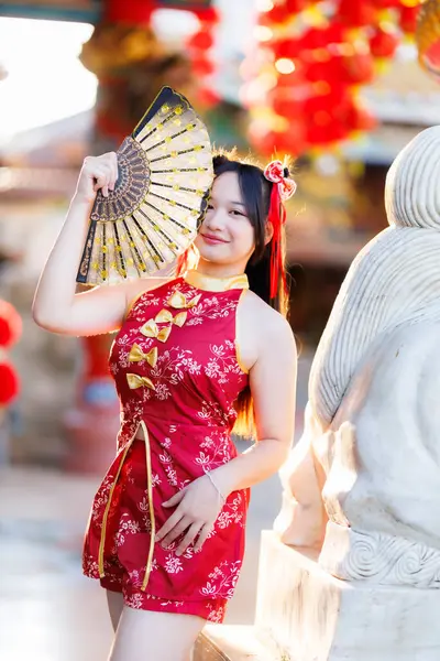 Güzel, şirin bir portre gülümseyen Asyalı genç bir kadın geleneksel Çin cheongsam süslemesi takıyor ve Tayland 'da Çin Yeni Yıl Festivali için Çin Fanning' i düzenliyor.