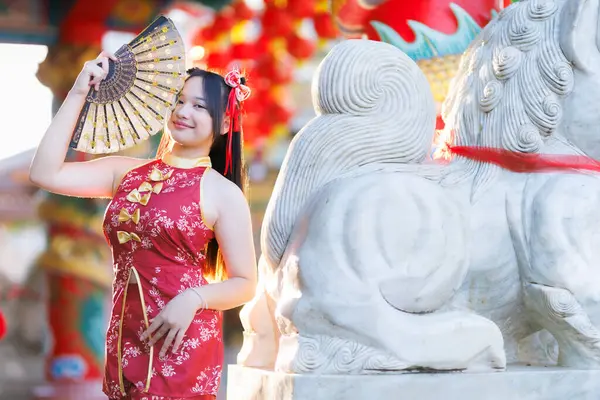 Güzel, şirin bir portre gülümseyen Asyalı genç bir kadın geleneksel Çin cheongsam süslemesi takıyor ve Tayland 'da Çin Yeni Yıl Festivali için Çin Fanning' i düzenliyor.