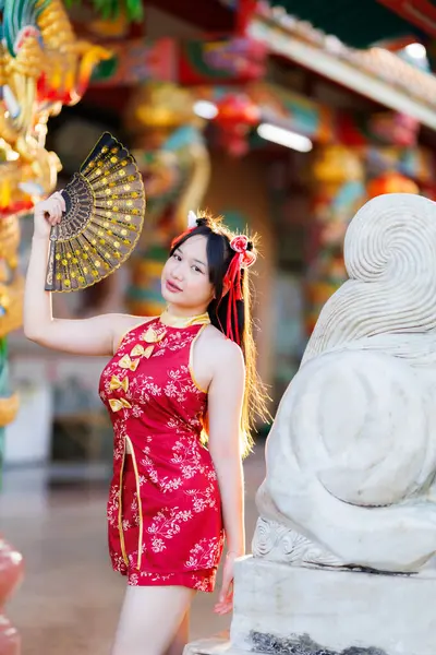 Güzel, şirin bir portre gülümseyen Asyalı genç bir kadın geleneksel Çin cheongsam süslemesi takıyor ve Tayland 'da Çin Yeni Yıl Festivali için Çin Fanning' i düzenliyor.