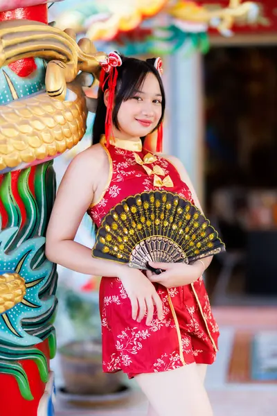 Güzel, şirin bir portre gülümseyen Asyalı genç bir kadın geleneksel Çin cheongsam süslemesi takıyor ve Tayland 'da Çin Yeni Yıl Festivali için Çin Fanning' i düzenliyor.