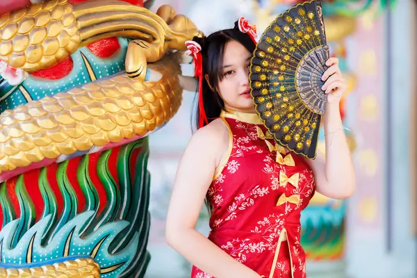 Güzel, şirin bir portre gülümseyen Asyalı genç bir kadın geleneksel Çin cheongsam süslemesi takıyor ve Tayland 'da Çin Yeni Yıl Festivali için Çin Fanning' i düzenliyor.