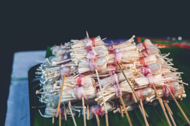 Muz yapraklarının üzerinde domuz dilimlerine sarılmış iğneli mantarlar. Sokak yemeği..