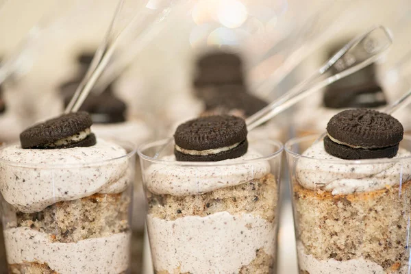 Rows of chocolate and whip cream desserts in little plastic cups with chocolate cookie toppings at dessert table