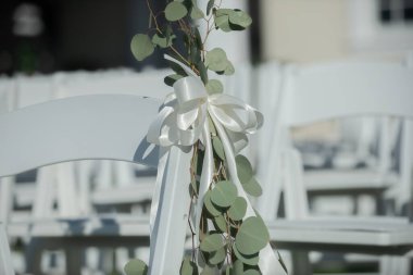 Düğün adasında beyaz kurdeleli beyaz sandalyeler ve yeşil bitkiler.