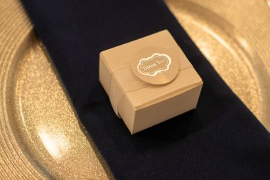 Dantele sarılı ahşap hediye kutusu ve altın tepside siyah peçeteye bir teşekkür etiketi.