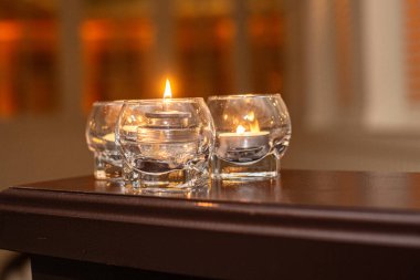 Üç cam, ahşap masada sıcak arka planda mumlar yakıyor.