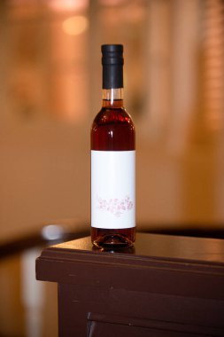 İnanılmaz bir kırmızı şarap şişesi, siyah kapaklı ve ahşap masada beyaz etiketli sıcak romantik arka planlı.