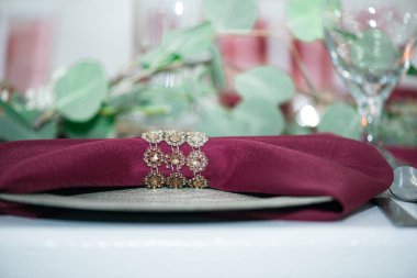 Süslü kırmızı peçete katlanmış, süslemeli peçete tutacağı zarif masa tabağında, yeşil arka planda, solda.