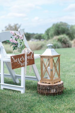 Amazing wood lantern with tin top resting on wood log near white chair with reserved sign at wedding ceremony isle clipart