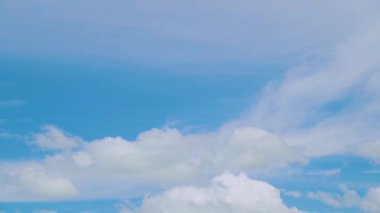 Gökyüzü açık mavi ve çok bulutlu. Gökyüzü çok parlak ve güneşli. Dağınık beyaz bulutlu mavi gökyüzü, doğa temalı bir arka plan için uygun, rahat bir atmosfer yaratır..