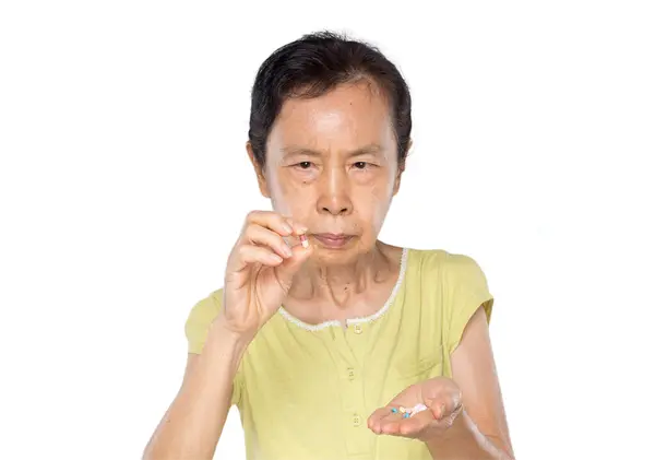 亚洲老妇人手里拿着白底药丸 图库照片