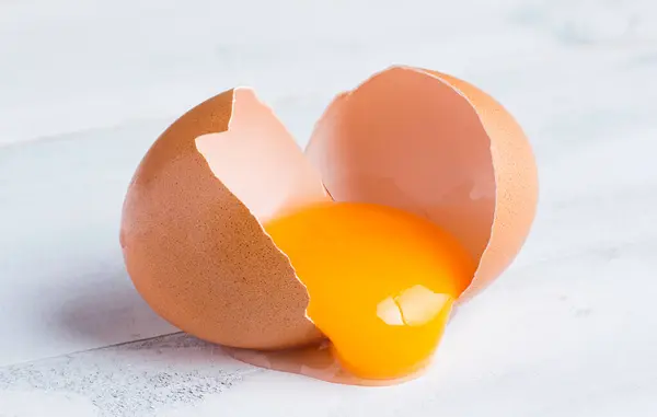 生破碎的鸡蛋 蛋黄在白色木壳上 图库照片