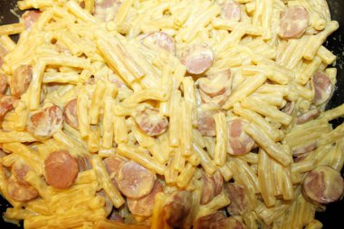 Tavada sosisli ve peynirli makarna pişirmek.