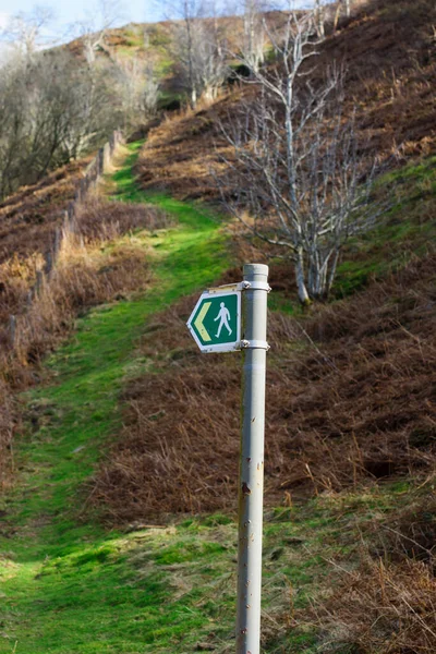 Rural sign post for hiking trails with a green grassy path leading up a British hillside