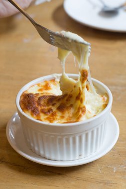Fork is scooping up cheese mashed potatoes in white cup on the wood table in restaurant.