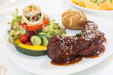 Pork ribs with barbecue sauce with vegetable salad on white plate on the dining table in restaurant.
