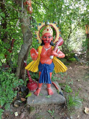 A Red-Colored Statue of Lord Hanuman at a Roadside Temple in India, Surrounded by Small Trees in the Background, Representing a Revered Hindu Deity with Cultural and Traditional Significance clipart