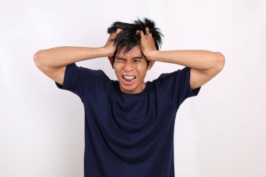 Stresli Asyalı genç adam bağırırken ve başını tutarken ayakta duruyor. Beyaz arkaplanda izole
