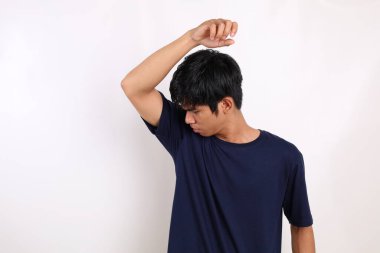 Asyalı genç adam koltukaltını koklarken ayakta duruyor. Kopyalama alanı ile beyaz arkaplanda izole.