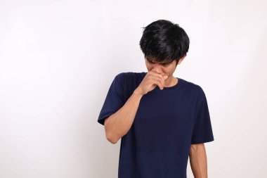 Asyalı genç adam burnunu kapatırken ayakta duruyor. Kötü koku konsepti. Beyaz arkaplanda izole